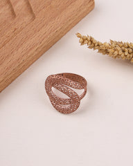 Rose gold filigree ring on a light surface with wooden block and dried plant