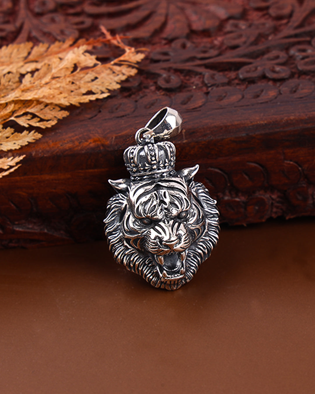 Silver tiger head pendant with a crown on a wooden surface