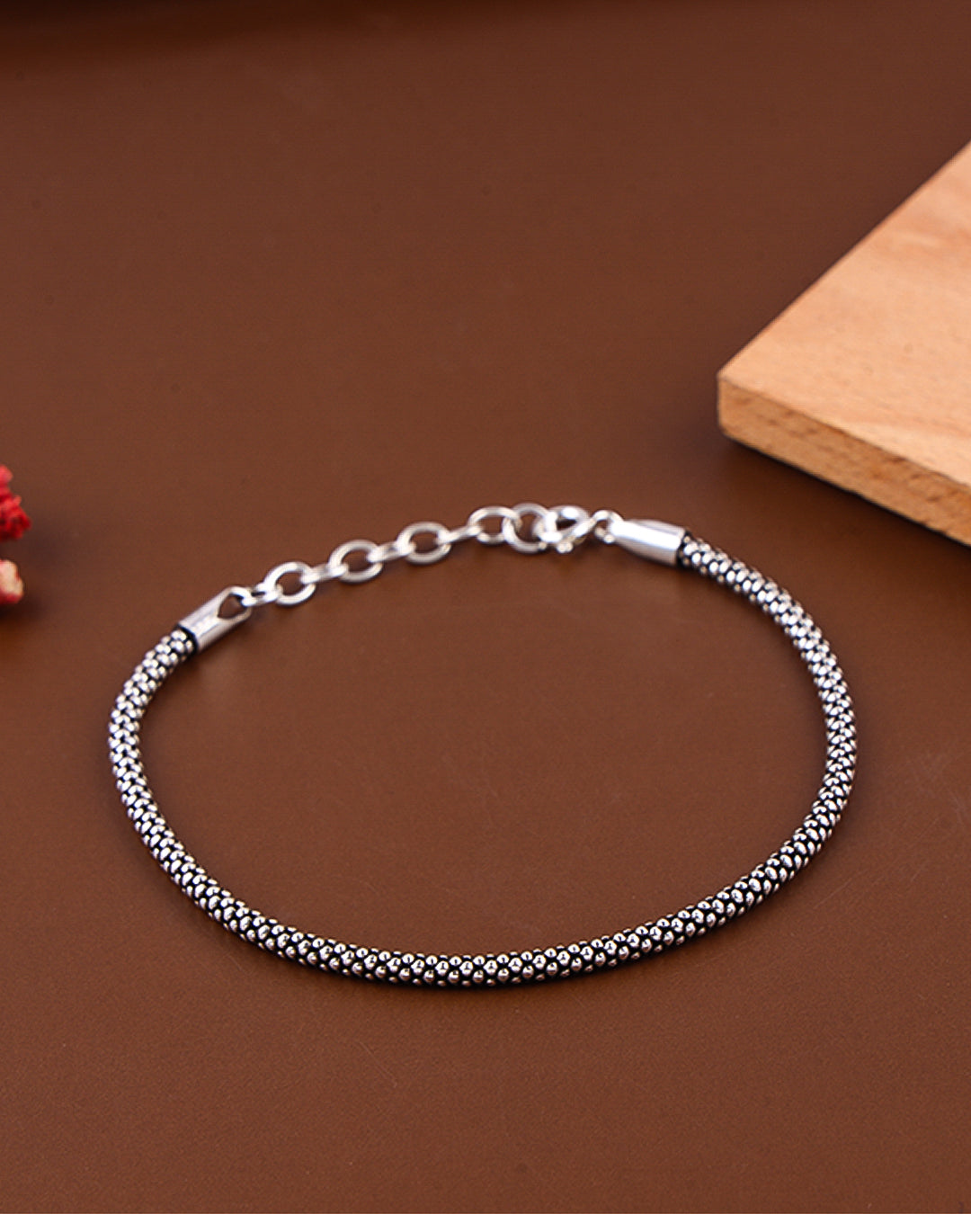 Silver bracelet on a brown surface with a wooden block in the background