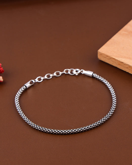 Silver bracelet on a brown surface with a wooden block in the background