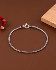 Silver braided bracelet on a brown surface with a wooden block and red flowers.