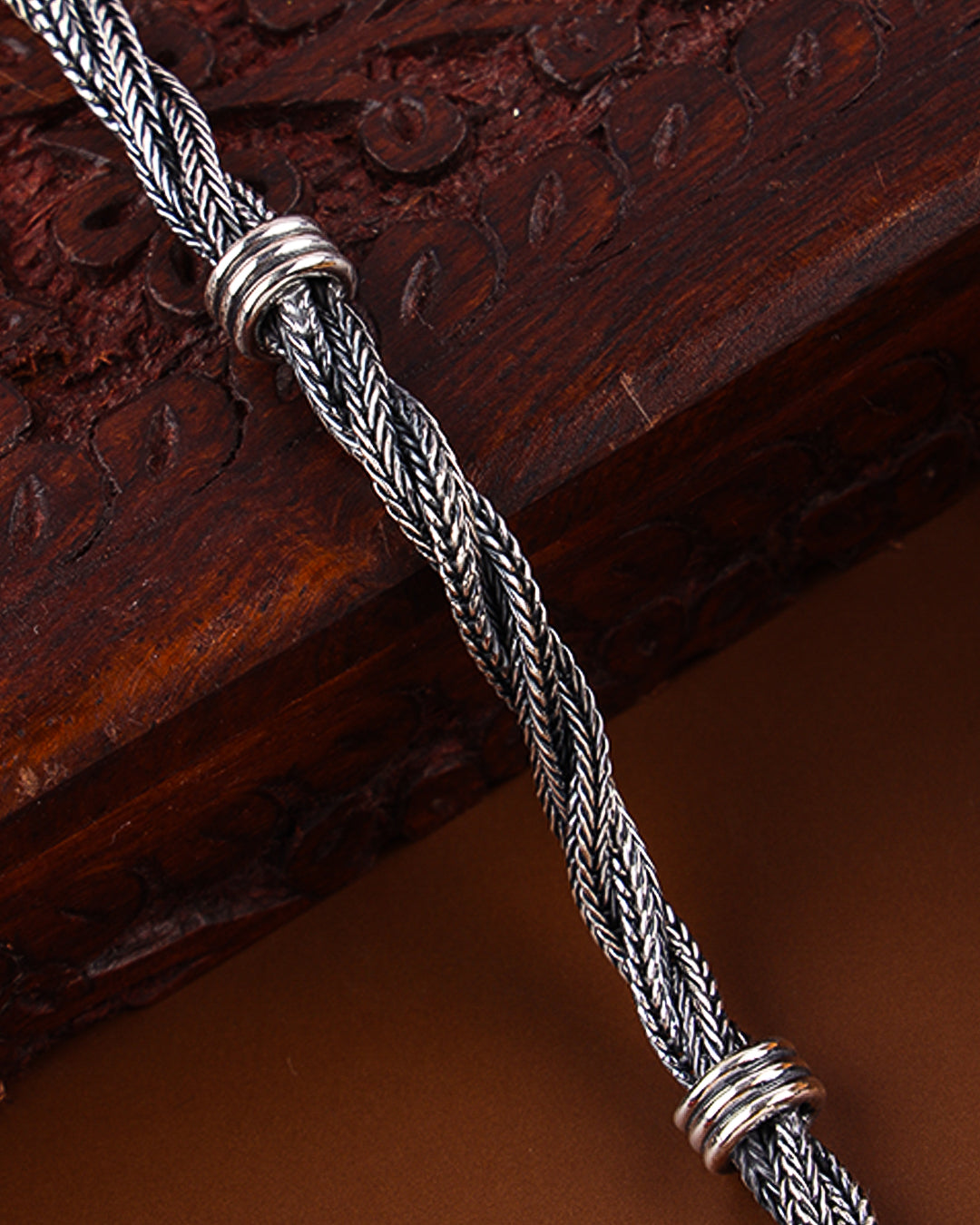 Silver braided cord with decorative ends on a wooden surface