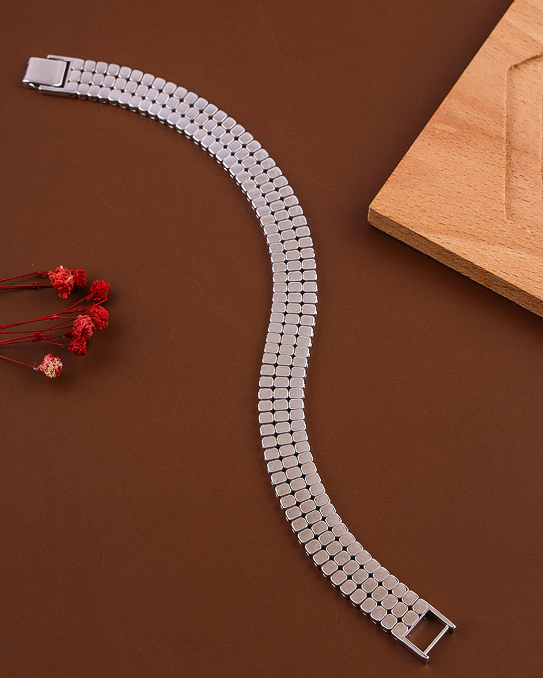 Silver watch strap on a brown surface with a wooden block and red flowers.