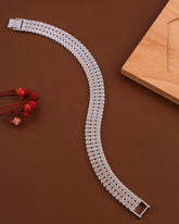 Silver watch strap on a brown surface with a wooden block and red flowers.