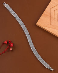 Silver bracelet on a brown surface with a wooden block and red flowers.