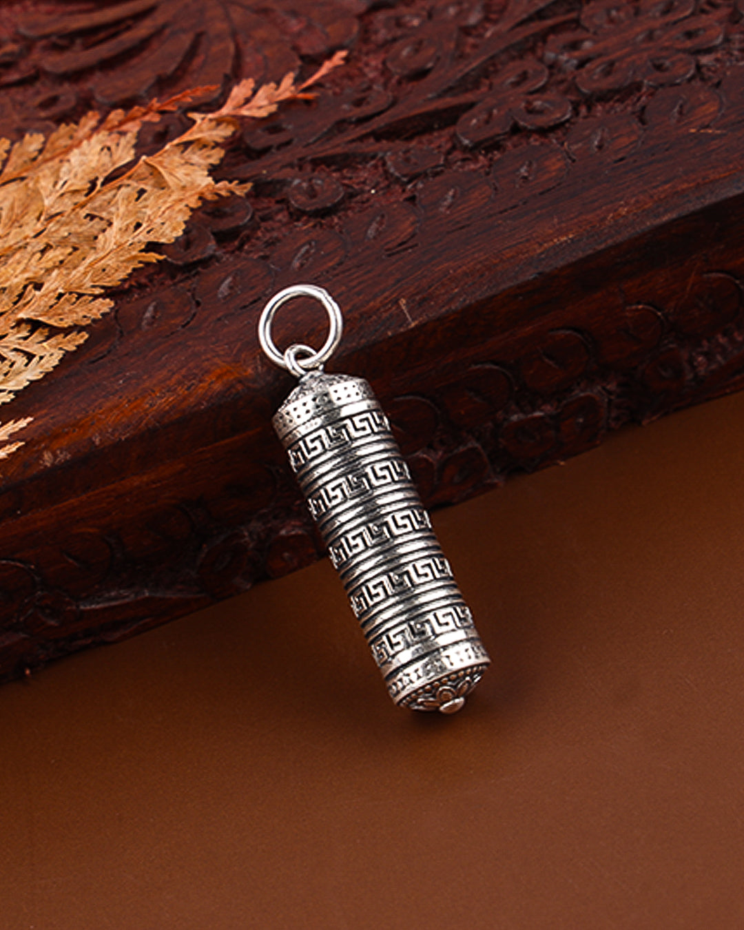 Silver cylindrical pendant with intricate design on a brown surface