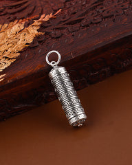 Silver cylindrical pendant with intricate design on a brown surface