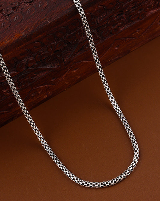 Silver chain necklace on a brown surface with a wooden box in the background