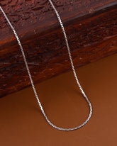 Silver chain necklace on a brown surface with a wooden box in the background
