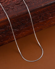 Silver chain necklace on a brown surface with a wooden box in the background
