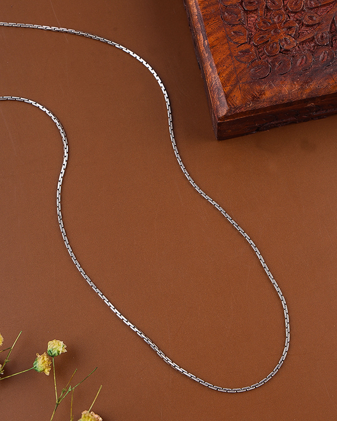 Silver chain on a brown surface with a wooden box and dried flowers.