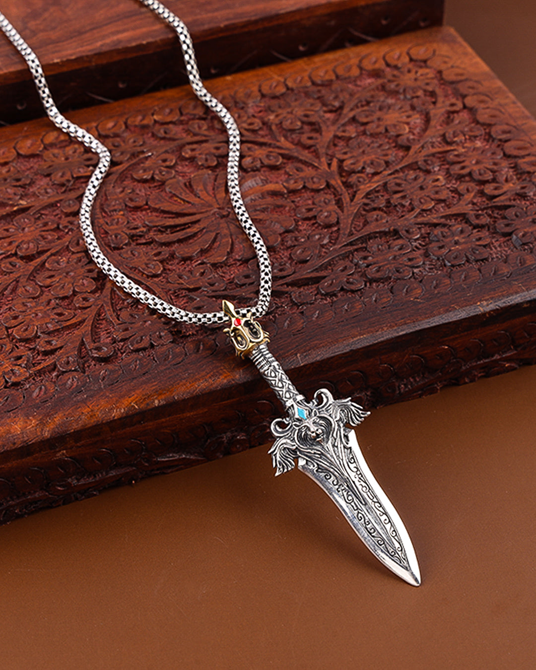 Silver dagger-shaped pendant on a chain against a wooden background