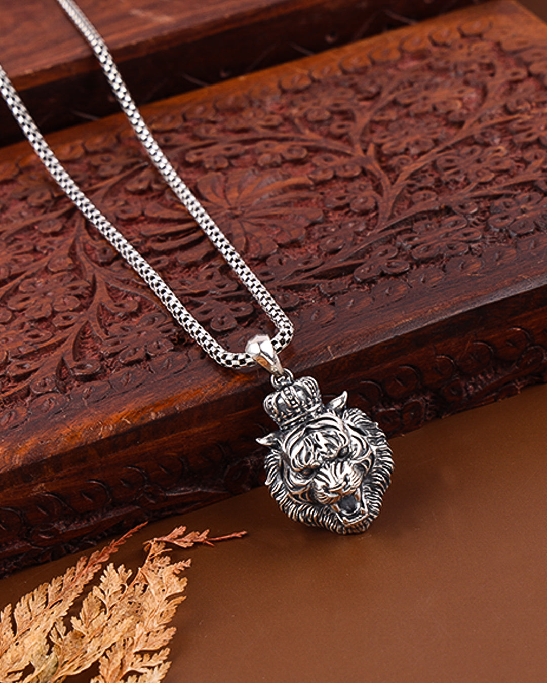 Silver necklace with a lion head pendant on a wooden surface
