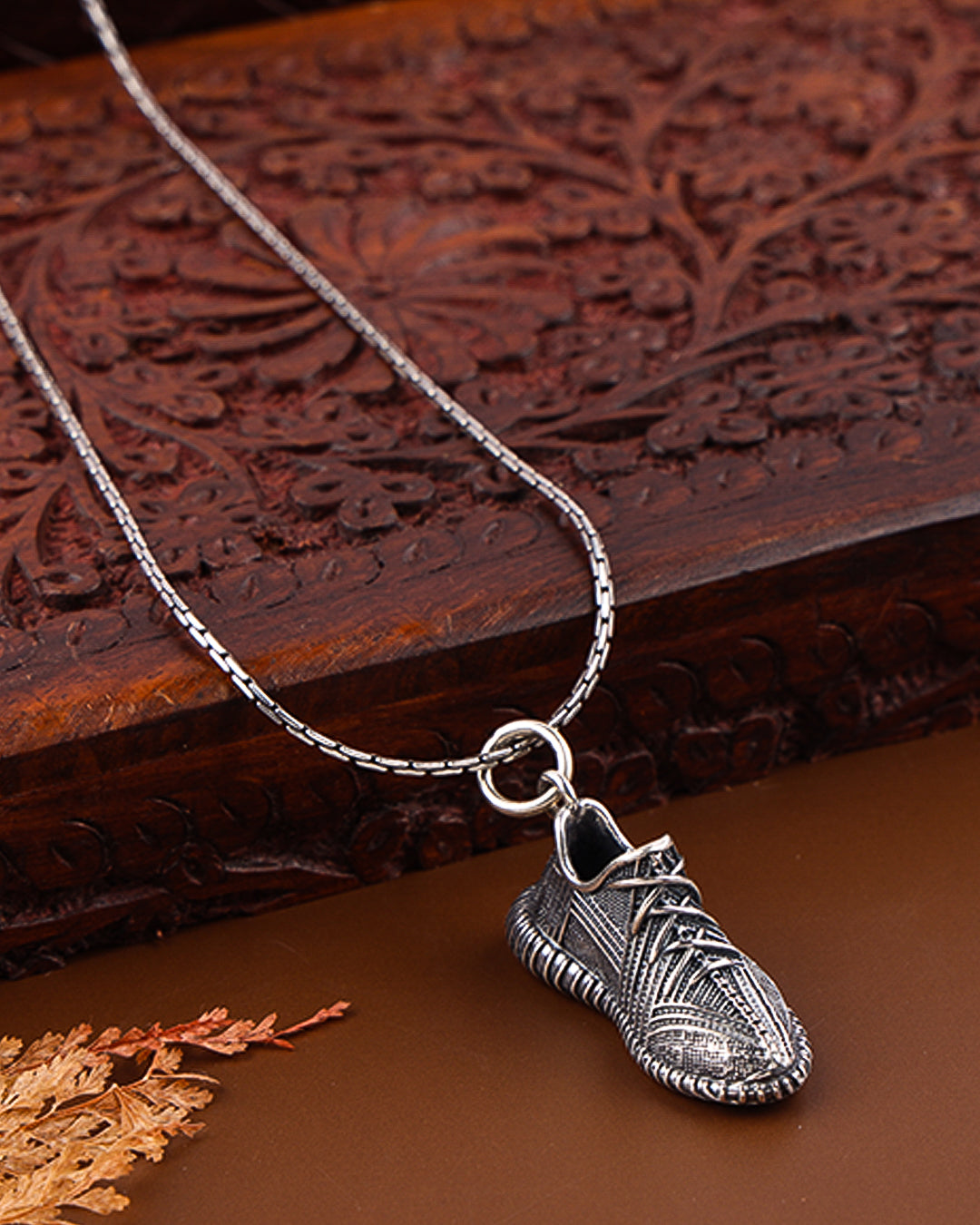 Silver shoe-shaped pendant on a chain against a wooden background