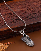 Silver shoe-shaped pendant on a chain against a wooden background