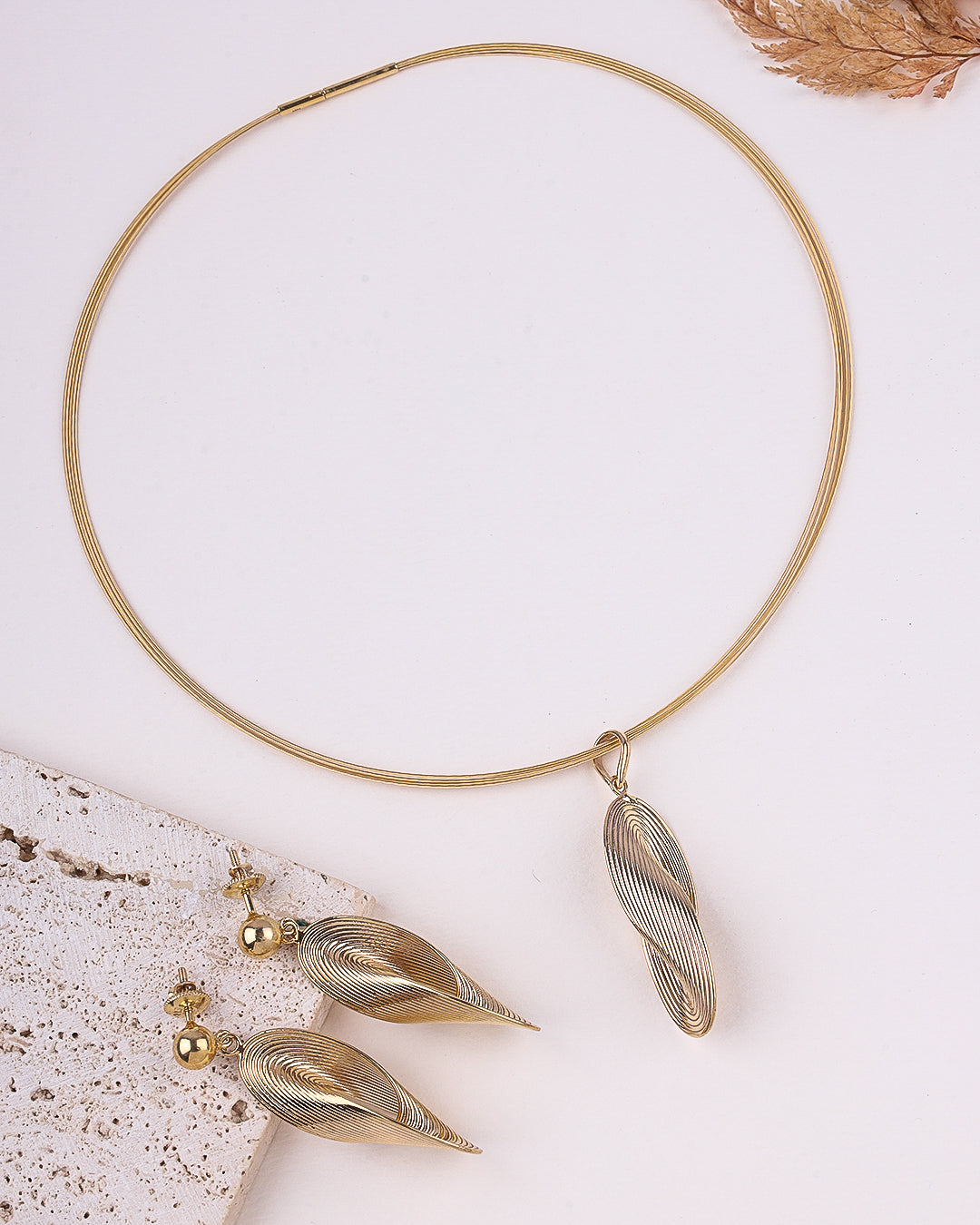 Gold necklace and earrings on a textured surface with a neutral background