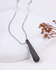 Necklace with a textured pendant on a white surface with dried flowers.