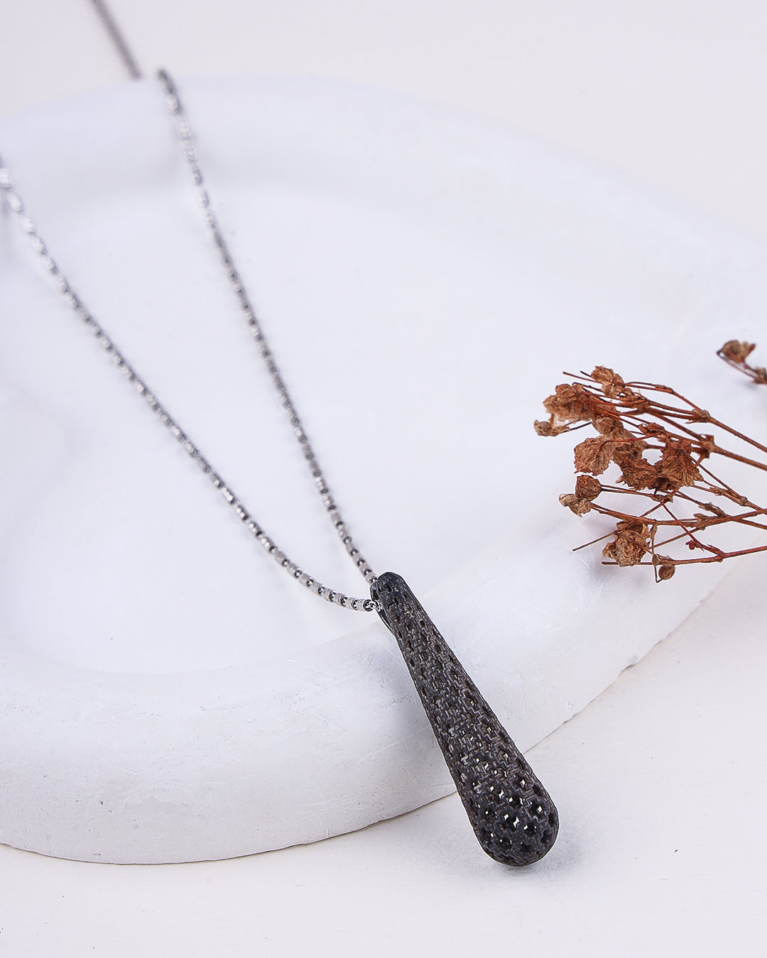 Necklace with a textured pendant on a white surface with dried flowers.