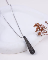 Necklace with a textured pendant on a white surface with dried flowers.