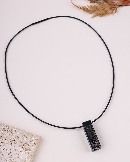 Black necklace with a pendant on a light surface