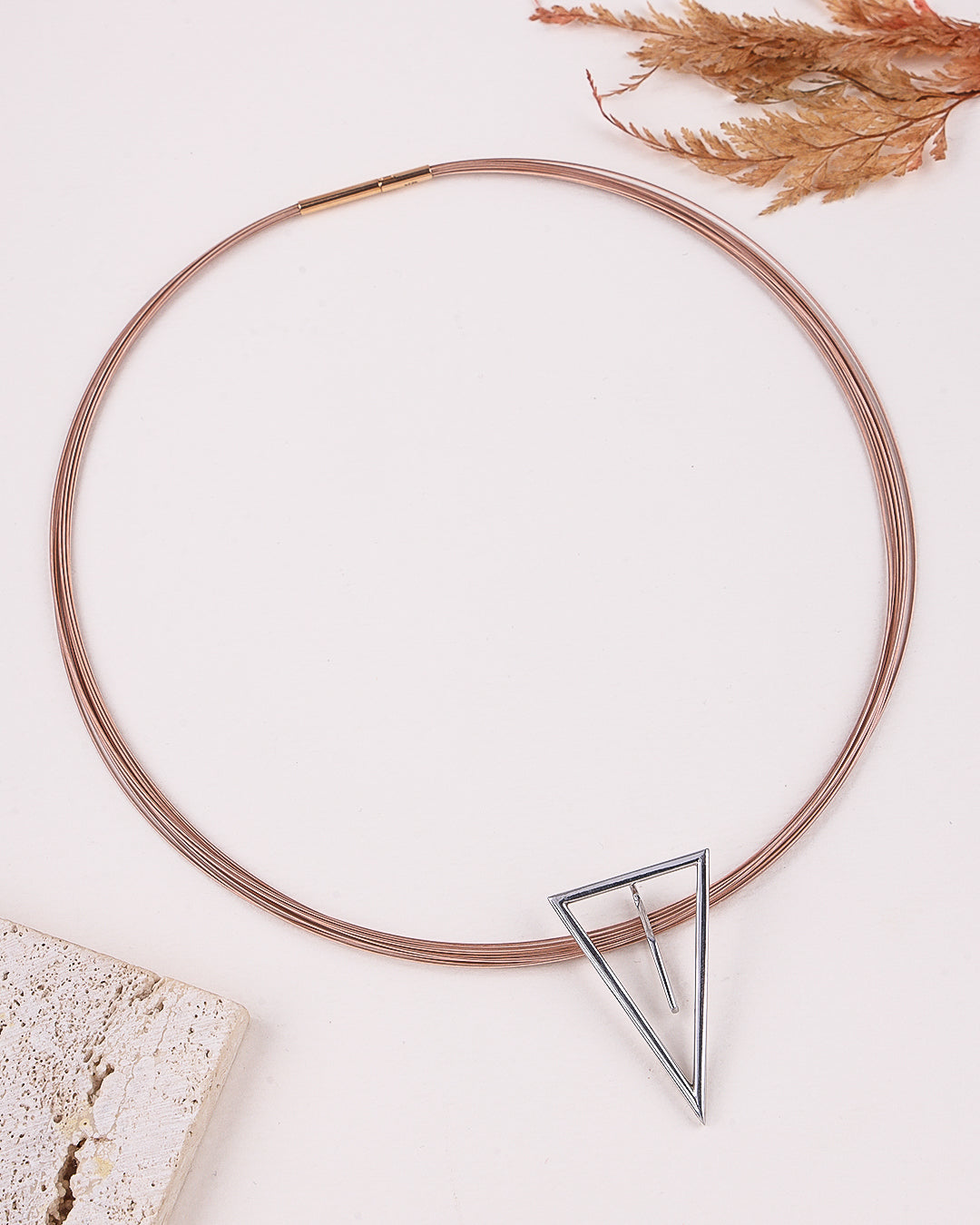 Rose gold necklace with a triangle-shaped clear stone on a light background