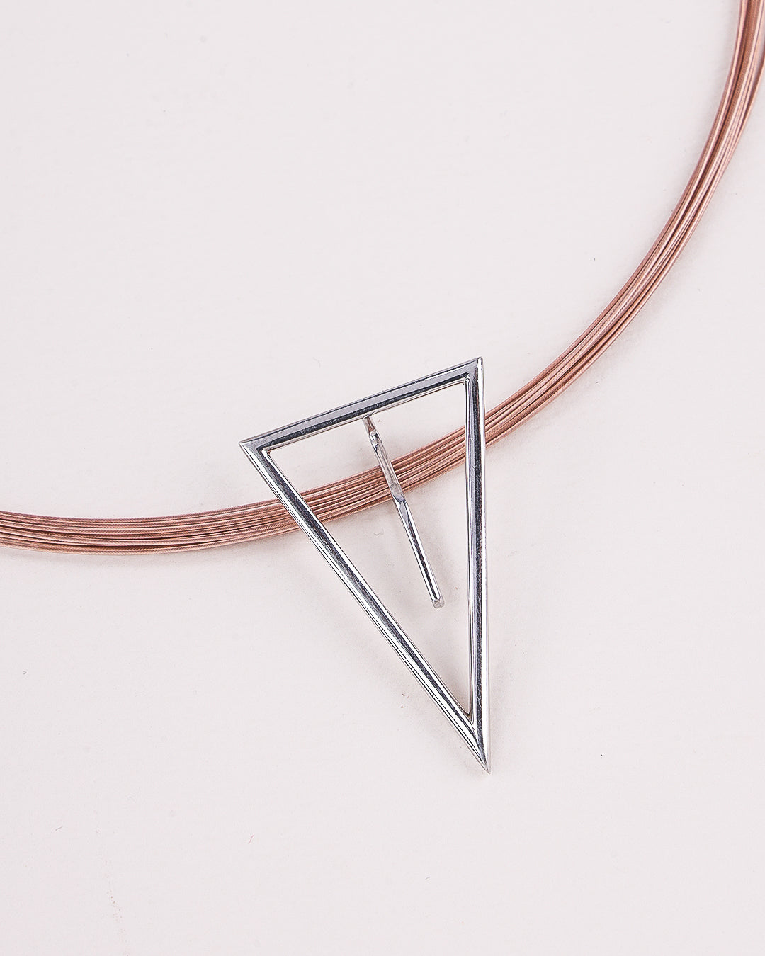 Silver triangle pendant on a pink wire against a light background