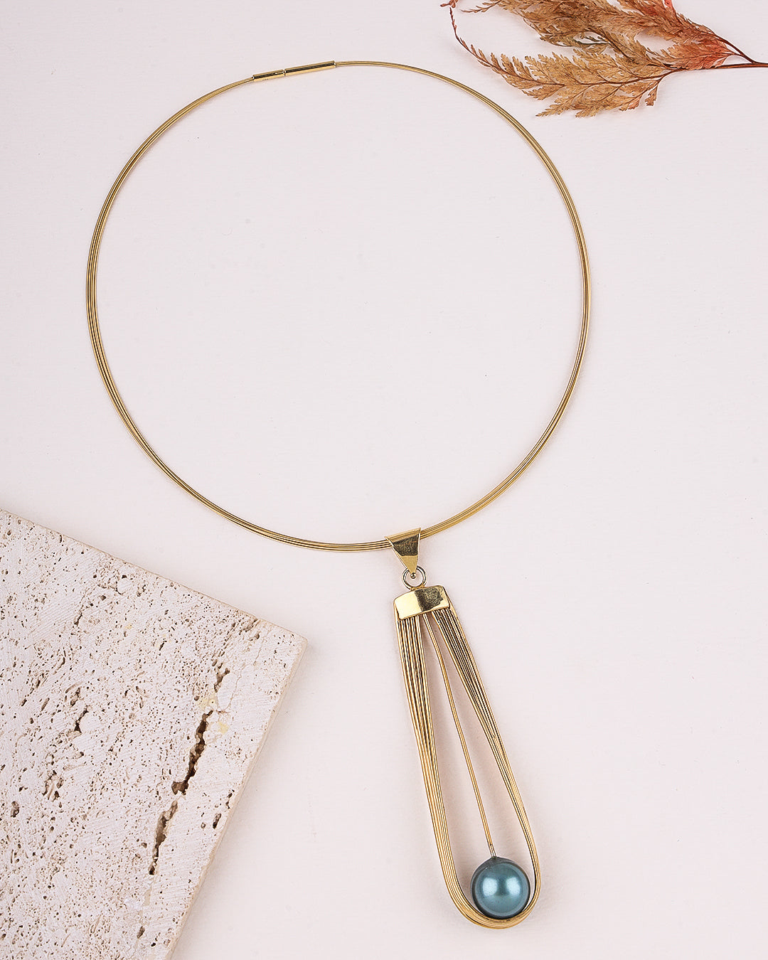 Gold necklace with a blue pendant on a light background