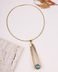 Gold necklace with a blue pendant on a light background