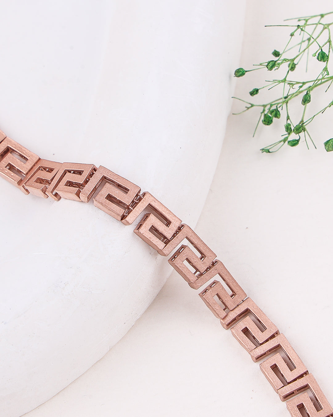 Rose gold bracelet on a white surface with greenery