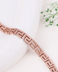 Rose gold bracelet on a white surface with greenery