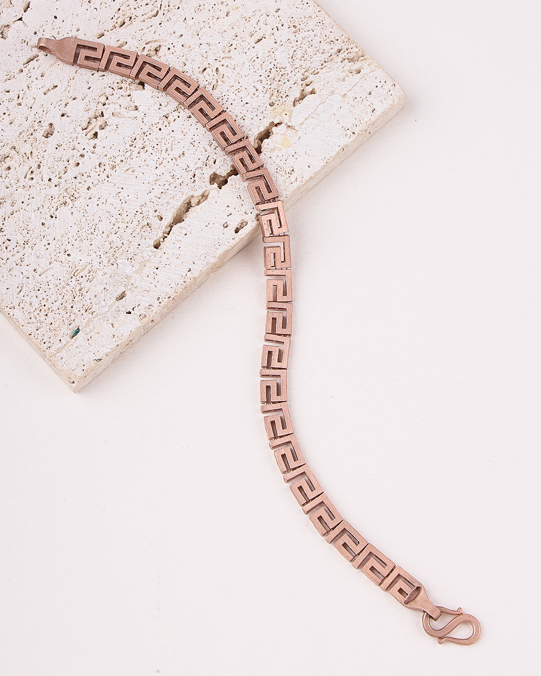 Rose gold bracelet with Greek key design on a light stone surface