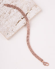 Rose gold bracelet with Greek key design on a light stone surface
