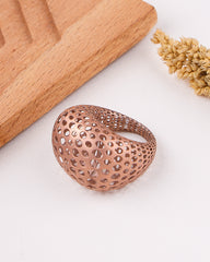 Matte rose gold ring on a white surface with a wooden cutting board and dried flowers in the background
