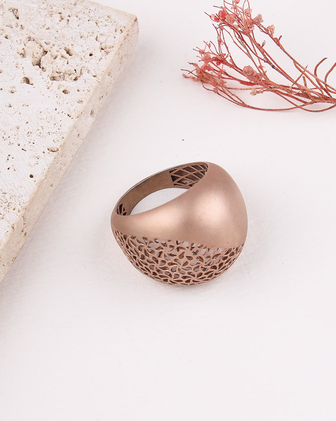 matte rose gold ring with intricate design on a light surface with decorative elements