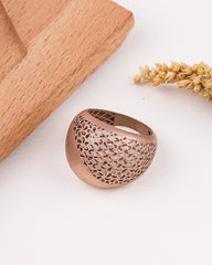 matte rose gold ring with intricate design on a light surface with wooden block and dried plants.