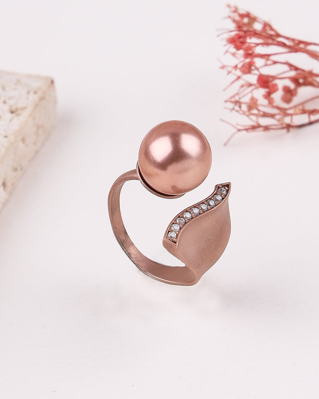 Rose gold ring with a spherical design and small stones on a light background