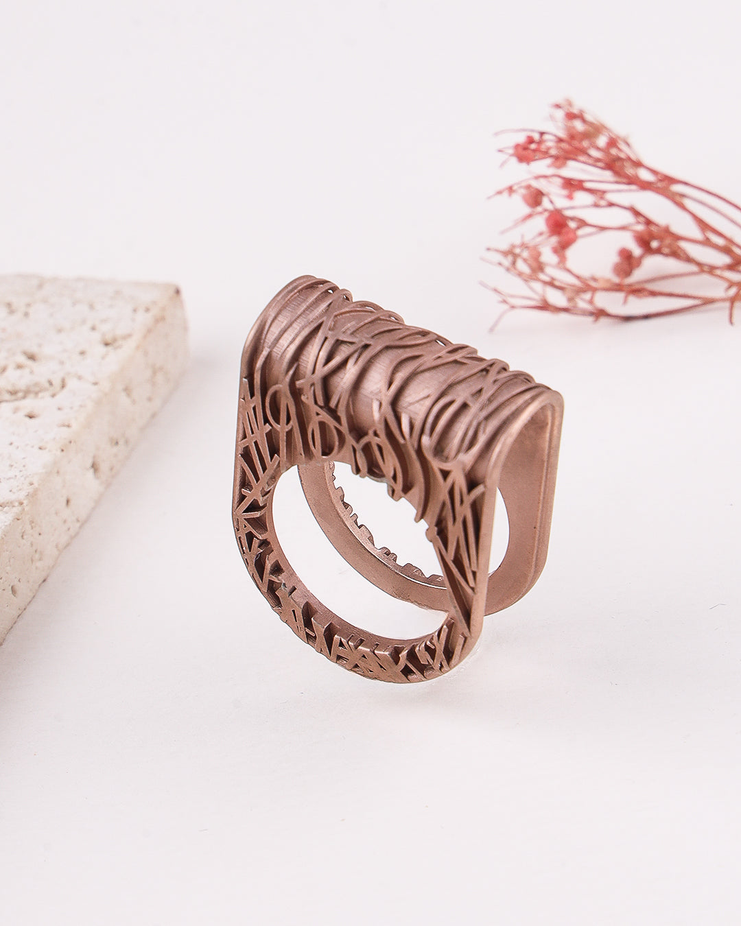 matte rose gold ring with intricate design on a light background