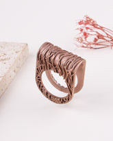 matte rose gold ring with intricate design on a light background