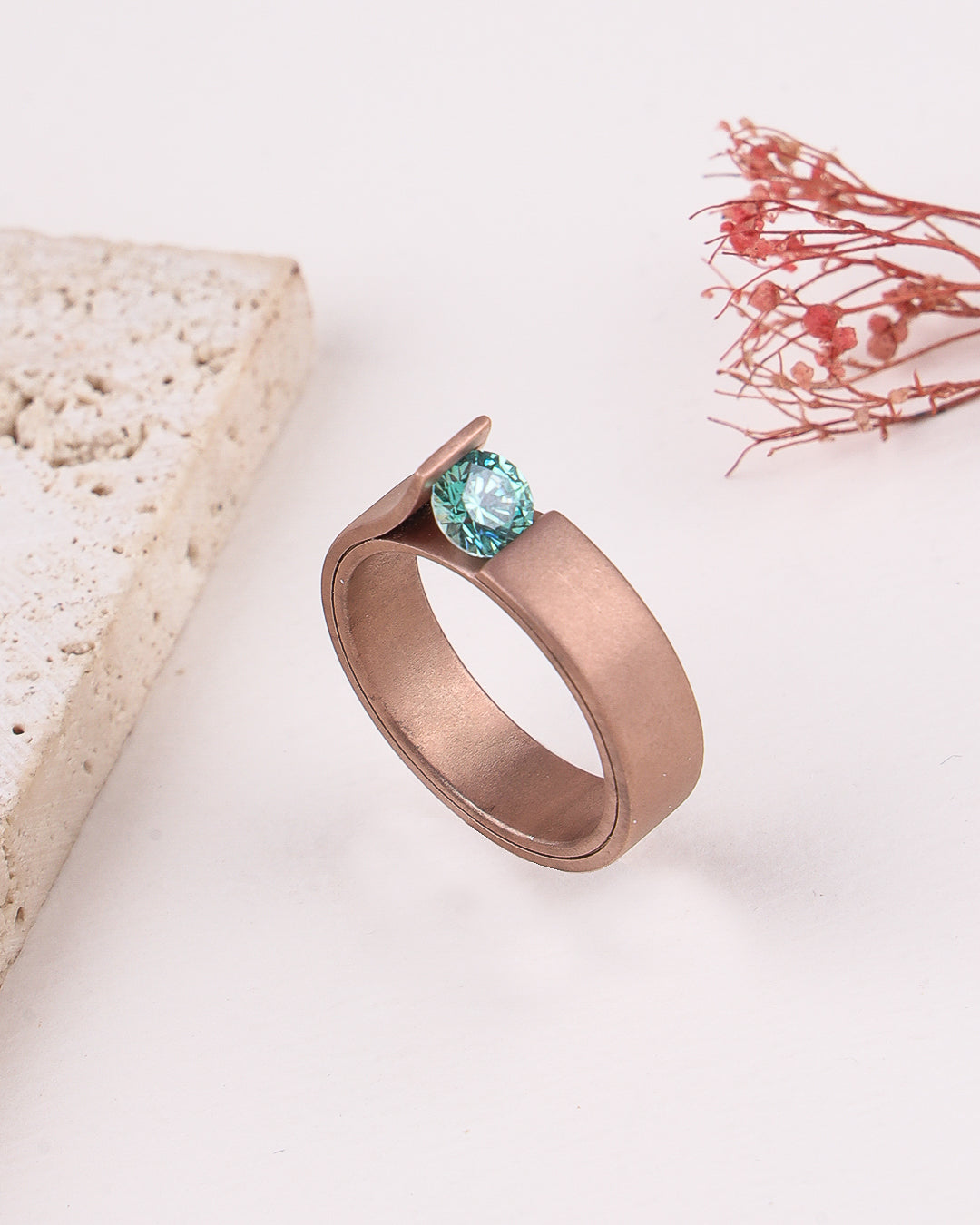 Rose gold ring with a green gemstone on a light background