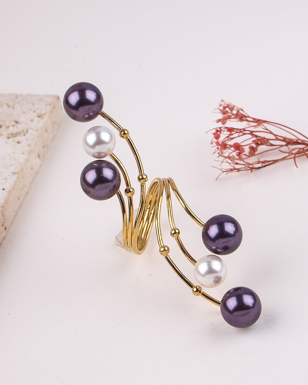 Gold ring with purple and white pearls on a light background