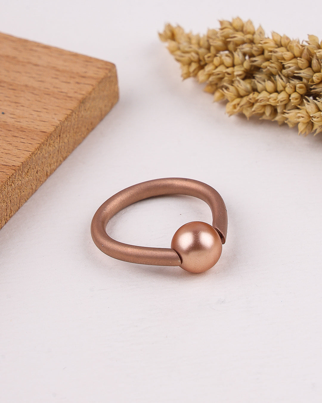 Rose gold ring with spherical end on a light surface with wooden block and dried lavender.
