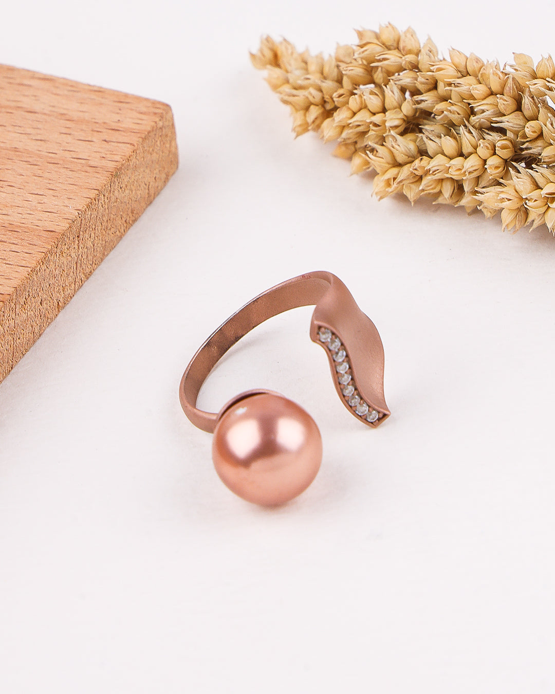 Rose gold ring with a pearl-like ball on a light background