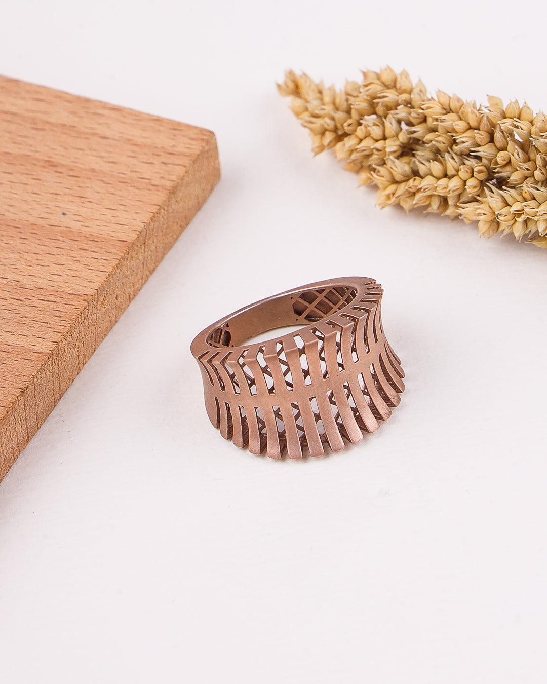 matte rose gold ring on a white surface with wooden block and dried wheat