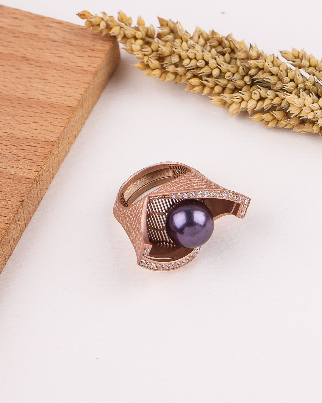 Rose gold ring with a purple gemstone on a white surface with wooden block and dried lavender.
