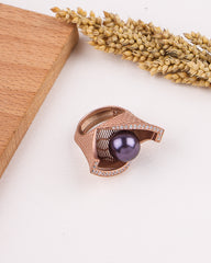 Rose gold ring with a purple gemstone on a white surface with wooden block and dried lavender.