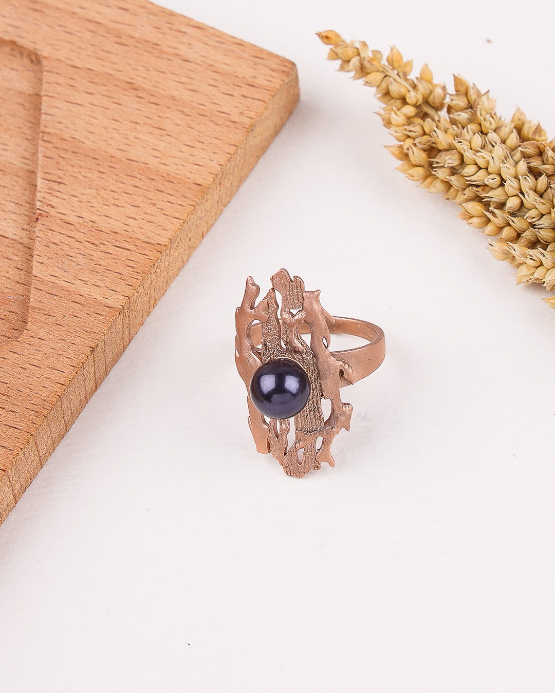 Rose gold ring with a black gemstone on a white surface with wooden and wheat elements.