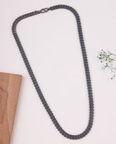 Black rhodium necklace on a light background with a wooden block and green leaves.