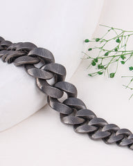 Black rhodium bracelet on a white surface with greenery