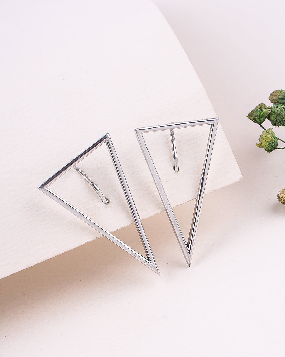 Silver triangle earrings on a white surface with a minimal background