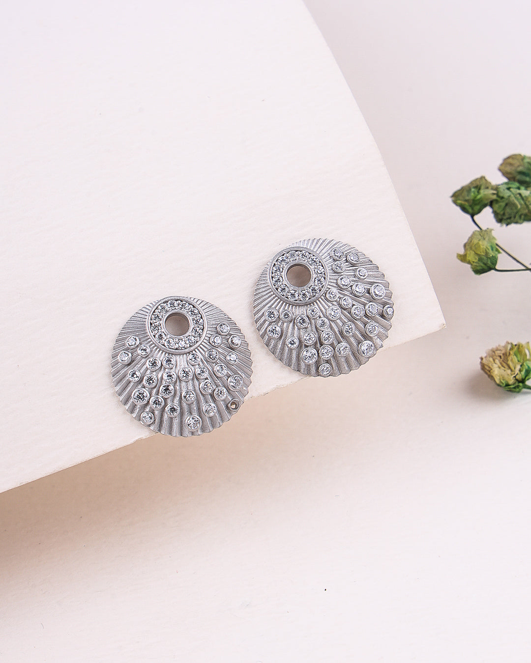 Pair of silver earrings on a light background with green flowers.